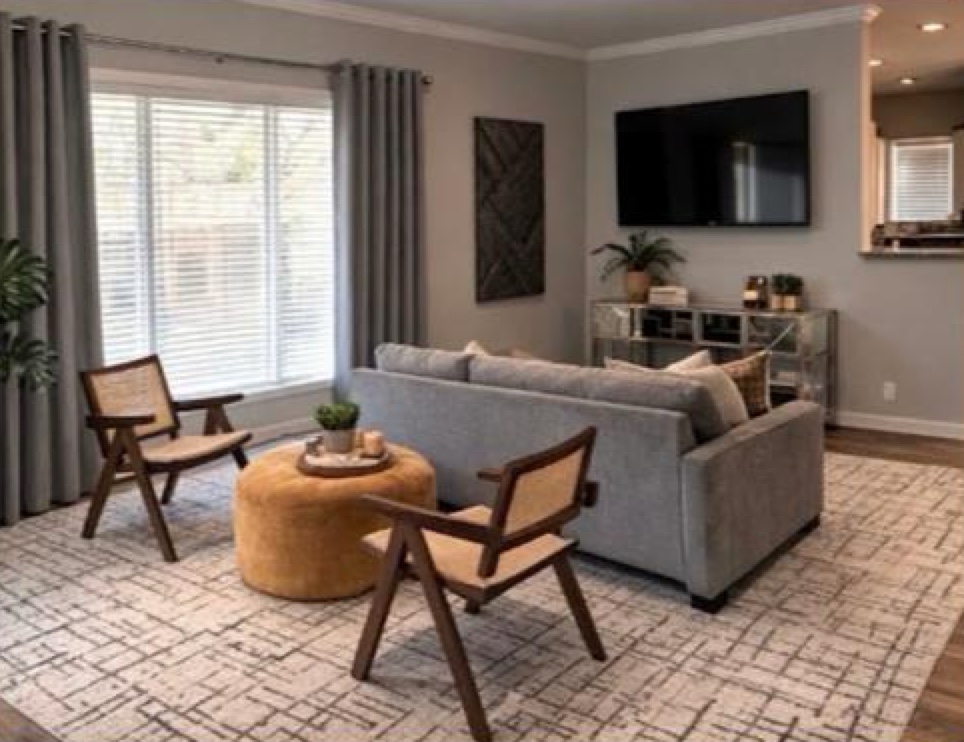 Furnished living room with gray sofa, woven accent chairs, and large windows