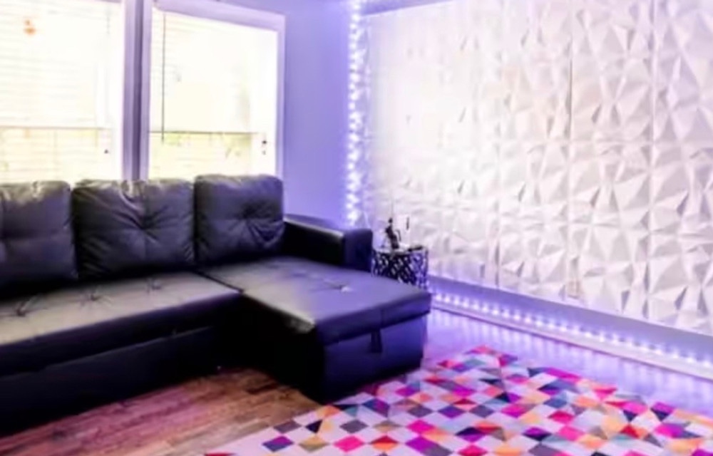 Living room with sectional sofa, 3D accent wall, and ambient lighting