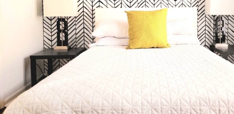 Private bedroom with herringbone accent wall, white quilt, and yellow pillow